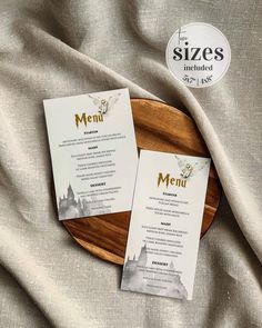 two menu cards sitting on top of a wooden platter next to a white cloth