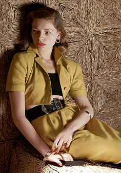 a woman sitting on top of a chair wearing a yellow dress and black belted shirt