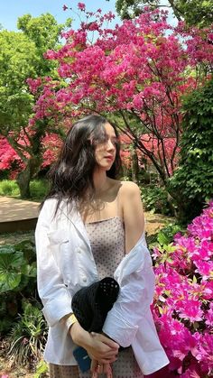 a woman standing in front of pink flowers holding a teddy bear and looking at the camera