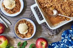 three bowls filled with apple crisp on top of a wooden table next to apples and spoons