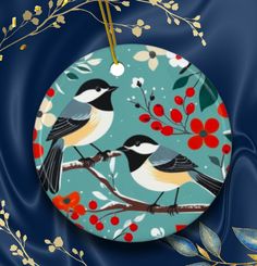 Description: Bird people rejoice! This ornament has chickadees, the socialites of the bird world. The artwork is a simple folk style rendition of chickadees, berries, and bright flowers on a steel blue background. I have other bird and critter ornaments and flags in my shop.  Makes a great gift for bird lovers, nature lovers, outdoor enthusiasts. If you have a request for a particular bird and art style. I am eager to make you a happy customer. Artwork made with help of AI. .: 0.125" (3mm) thick high-quality ceramic .: Glossy finish .: One-sided print .: Hole and gold-toned hanging string included Cottagecore Christmas Tree, Cottagecore Christmas, Bird People, Christmas Craft Fair, Bird Watchers, Hand Painted Stones, Folk Fashion, Bird Decor