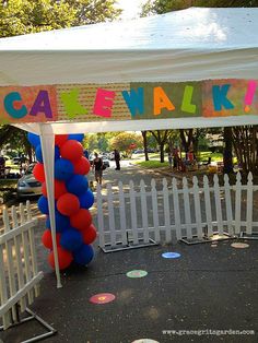 a white fence with a sign that says cakewalk on it and balloons hanging from the top