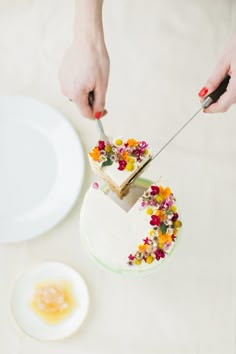 two people cutting into a cake with flowers on it and an egg in the background