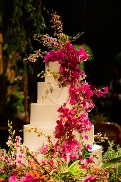 a white wedding cake with pink flowers and greenery on top is surrounded by greenery