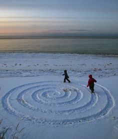 two children are playing in the snow by the ocean with a spiral design on it