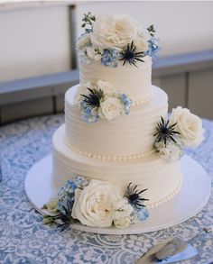 a three tiered wedding cake with blue and white flowers on it's side