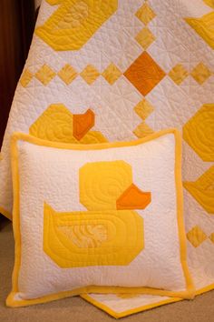 two quilted pillows with yellow ducks on them next to a white and yellow quilt