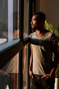 a man standing next to a window with his hands on the windowsill looking out