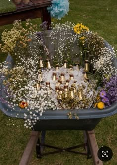 a wheelbarrow filled with lots of bottles and flowers on top of green grass