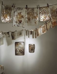 some pictures hanging on a clothes line in front of a white wall with rust stains