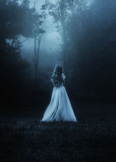 a woman in a white dress standing in the dark woods