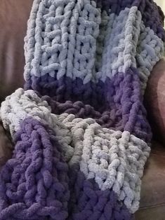 a purple and white crocheted blanket sitting on top of a brown leather chair