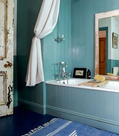 a bathroom with blue walls and white bathtub next to a mirror on the wall