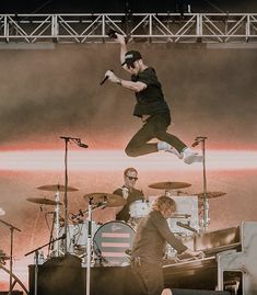 a man jumping in the air on top of a stage next to two drummers