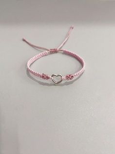 a pink string bracelet with a heart charm on it's end, sitting on a white surface