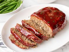 sliced meatloaf on a plate with green beans and mashed potatoes in the background