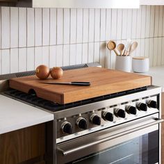 a wooden cutting board sitting on top of a stove next to utensils and spoons