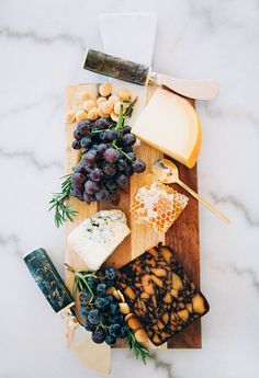 various cheeses and crackers on a cutting board with grapes, nuts and herbs