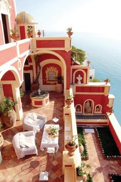 an outdoor patio with chairs and tables next to the ocean in front of a red building