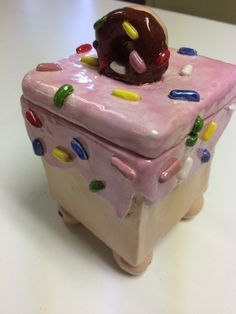 a small pink box with a chocolate covered doughnut on it's top and sprinkles all over the surface