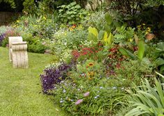 a garden filled with lots of different types of flowers and plants next to a wooden bench