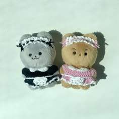 two small stuffed animals sitting next to each other on a white surface with one bear wearing a dress