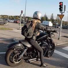 a woman riding on the back of a motorcycle down a street next to traffic lights