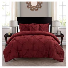 a bed with red comforter and pillows in a room next to two framed pictures