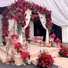 an outdoor wedding setup with red flowers and white drapes on the stage, surrounded by pink chairs