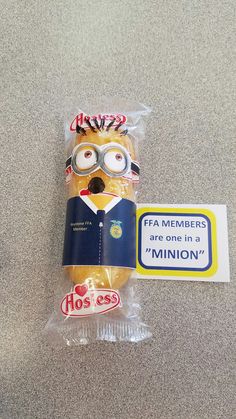 a minion is wrapped in plastic and sitting next to a sticker that says fa members are one in a minion