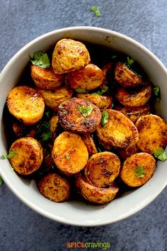 a white bowl filled with cooked potatoes on top of a blue tablecloth and green leaves