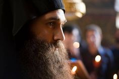 a man with a long beard wearing a black hat and holding a lit candle in his hand