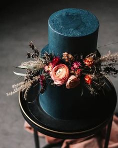 a blue top hat with flowers and feathers is sitting on a small black table next to a brown cloth