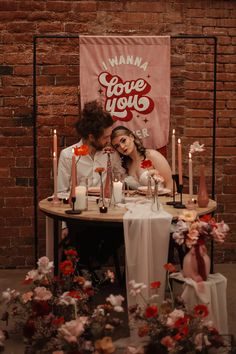 a man and woman sitting at a table in front of a sign that says i love you