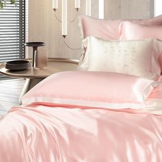 a bed with pink sheets and pillows in a room next to a lamp on a table