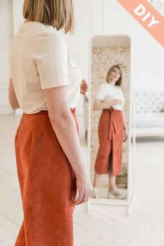 a woman standing in front of a mirror wearing an orange skirt and white shirt with her hands on her hips