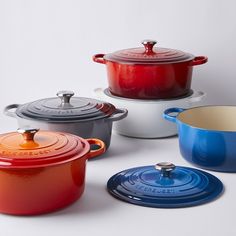 several different colored pots and pans on a white surface