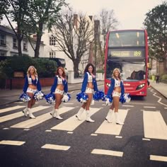 the cheerleaders are crossing the street in front of a double - decker bus