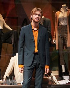 a man standing in front of mannequins wearing suit and orange shirt on display