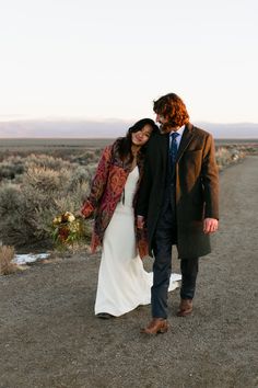 a man and woman walking down a dirt road in the middle of nowhere, holding hands