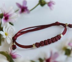 a red cord bracelet with gold beads and flowers on the table next to white flowers