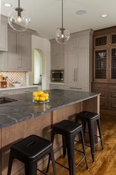 a large kitchen with marble counter tops and wooden flooring that has stools in front of it