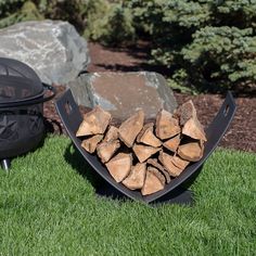 a fire pit sitting on top of a lush green field next to a pile of logs