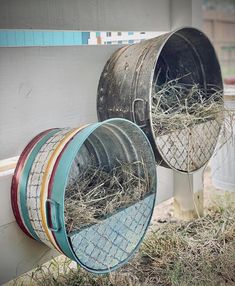 three metal buckets filled with hay sitting on the side of a white fence