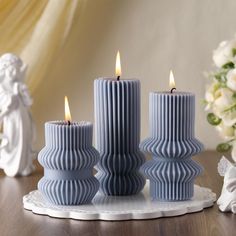 three blue candles sitting on top of a table next to white flowers and angel figurines