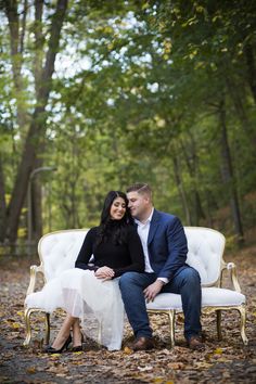 a man and woman sitting on a white couch in the middle of a forest with leaves all around them