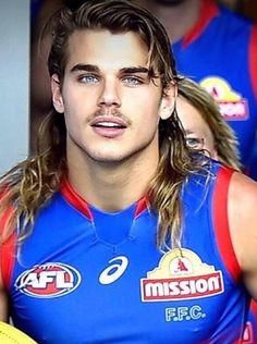 a man with long hair and blue jersey holding a yellow frisbee