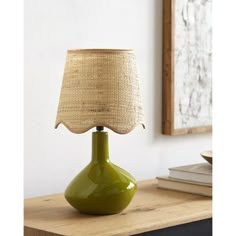 a green lamp sitting on top of a table next to a book shelf and framed artwork