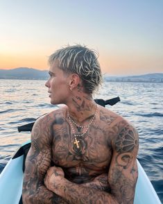 a man with tattoos on his chest sitting in a boat looking out at the water