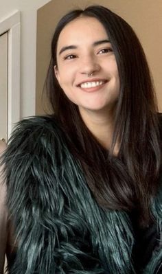 a woman with long hair wearing a fur vest and smiling at the camera while standing in front of a door